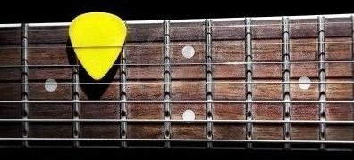 15478656-yellow-guitar-pick-on-the-fingerboard-close-up-isolated-on-black-background